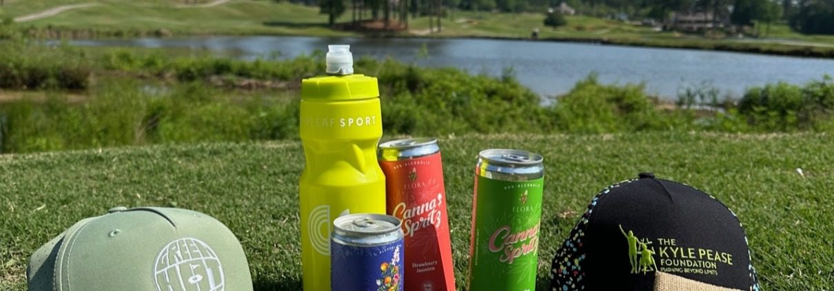 A Green Hat Classic golf hat on a grassy golf course surrounded with beverages.