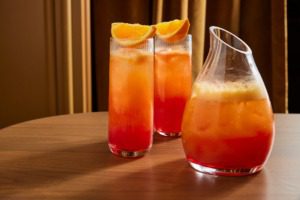 Glasses with orange beverage sitting on table next to decanter