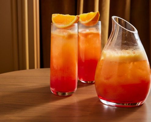 Glasses with orange beverage sitting on table next to decanter
